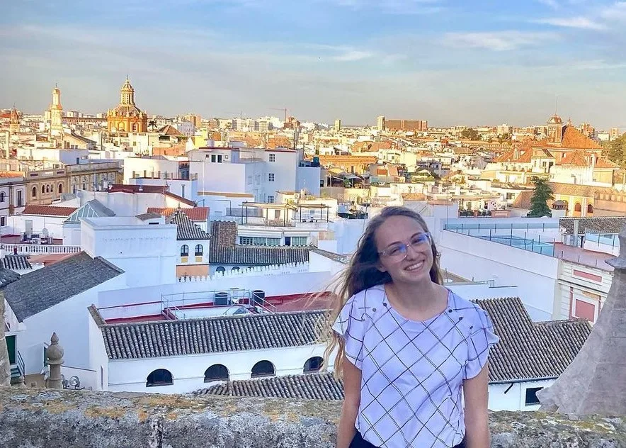 Smiling woman on rooftop overlooking city with domed buildings.