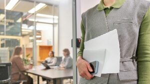 Professional holding a laptop outside a glass office meeting room