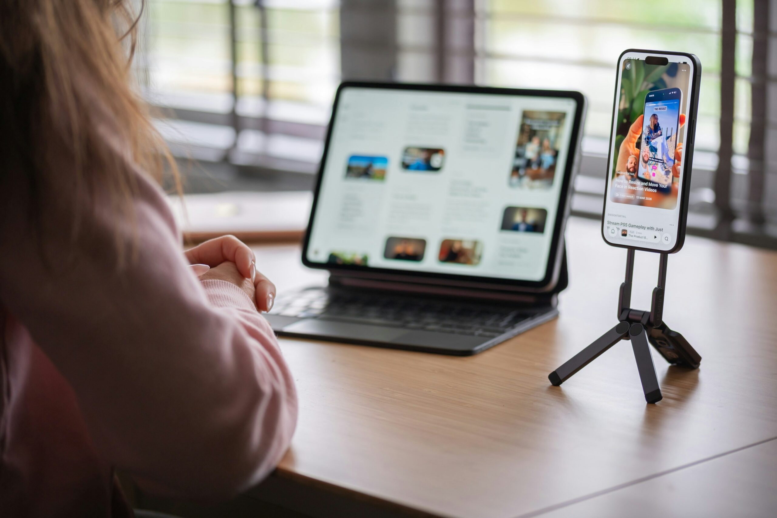 Marketing intern working on social media content using a smartphone and tablet at a desk