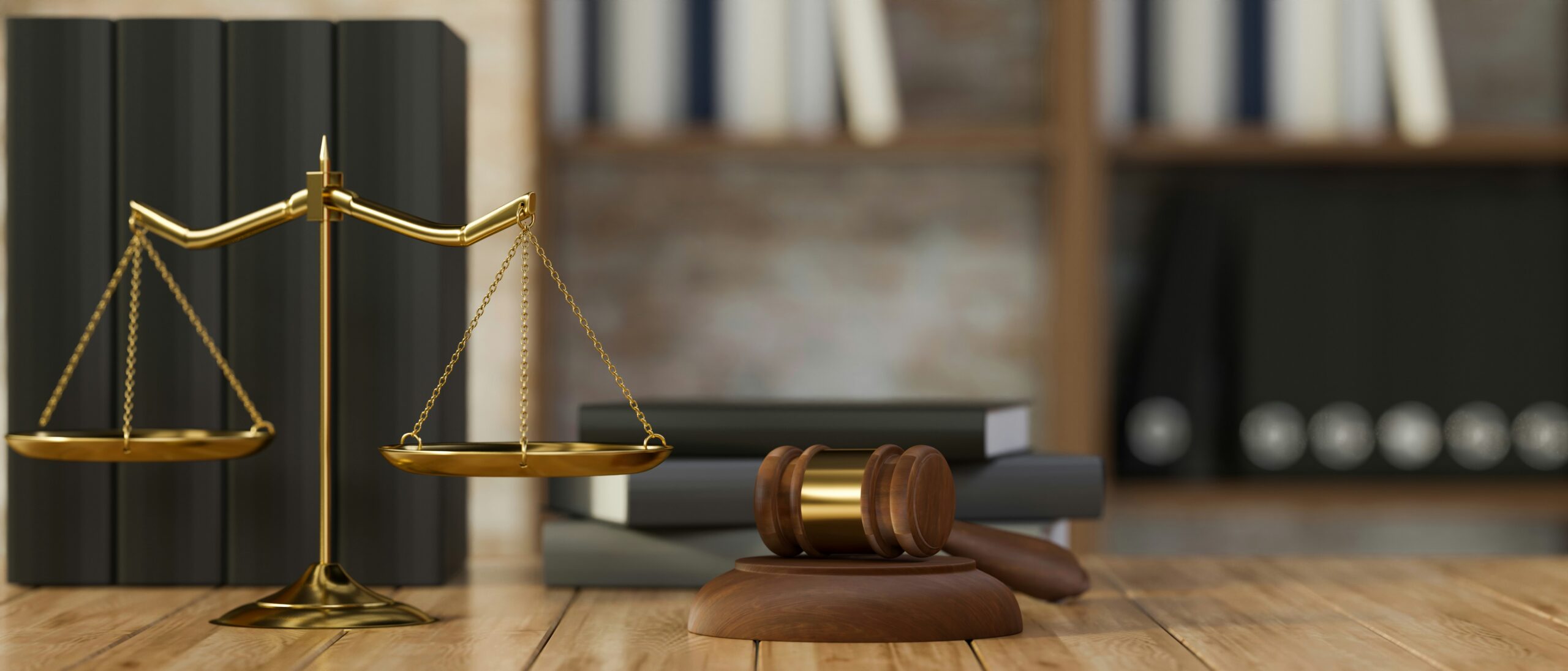 Golden scales of justice paired with a wooden judge's gavel on a wooden desk with law books in the background.