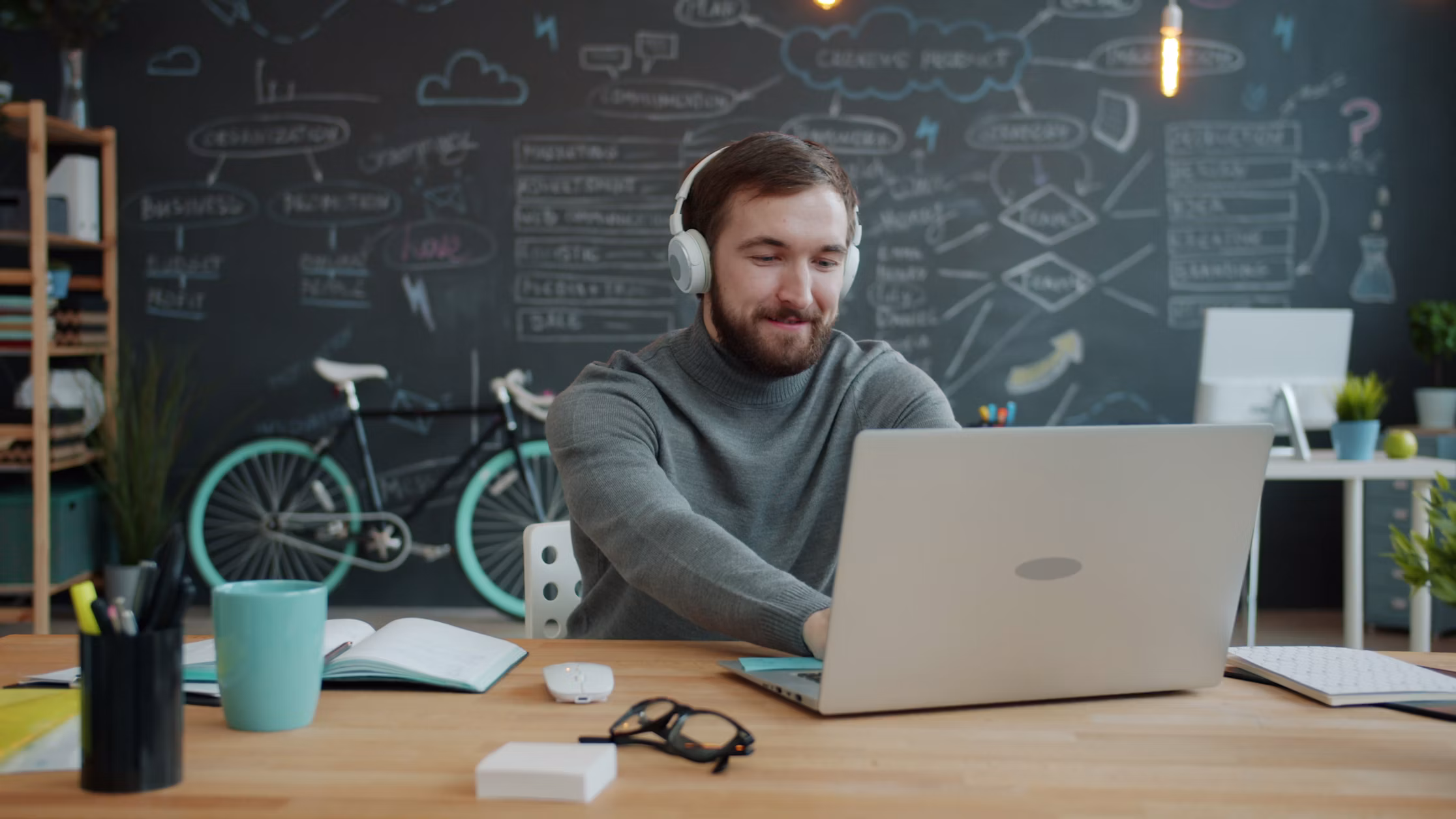 Man using a laptop at a desk in a creative office with a chalkboard wall behind him