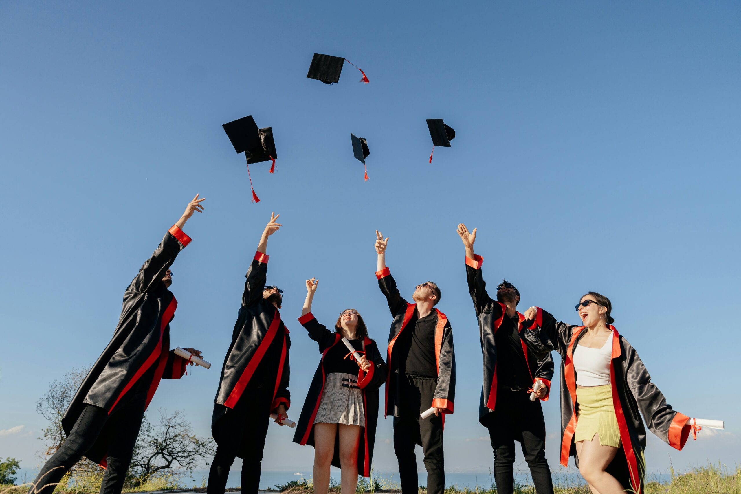 Graduates in caps and gowns throwing mortarboards in the air, representing students applying to graduate school.