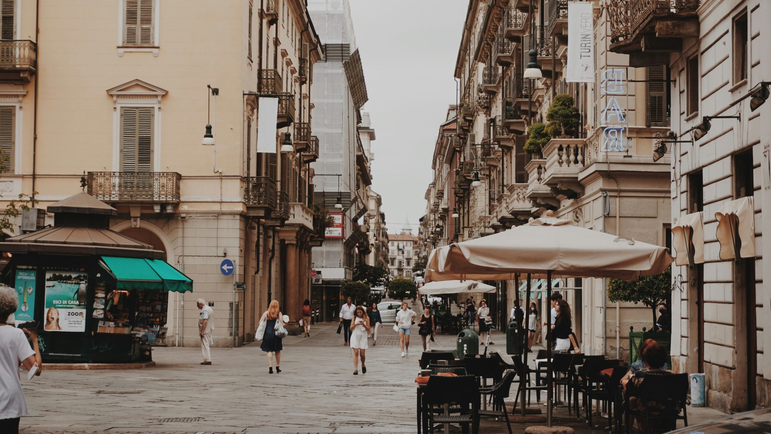 Pedestrians walking through a European city street with outdoor cafes