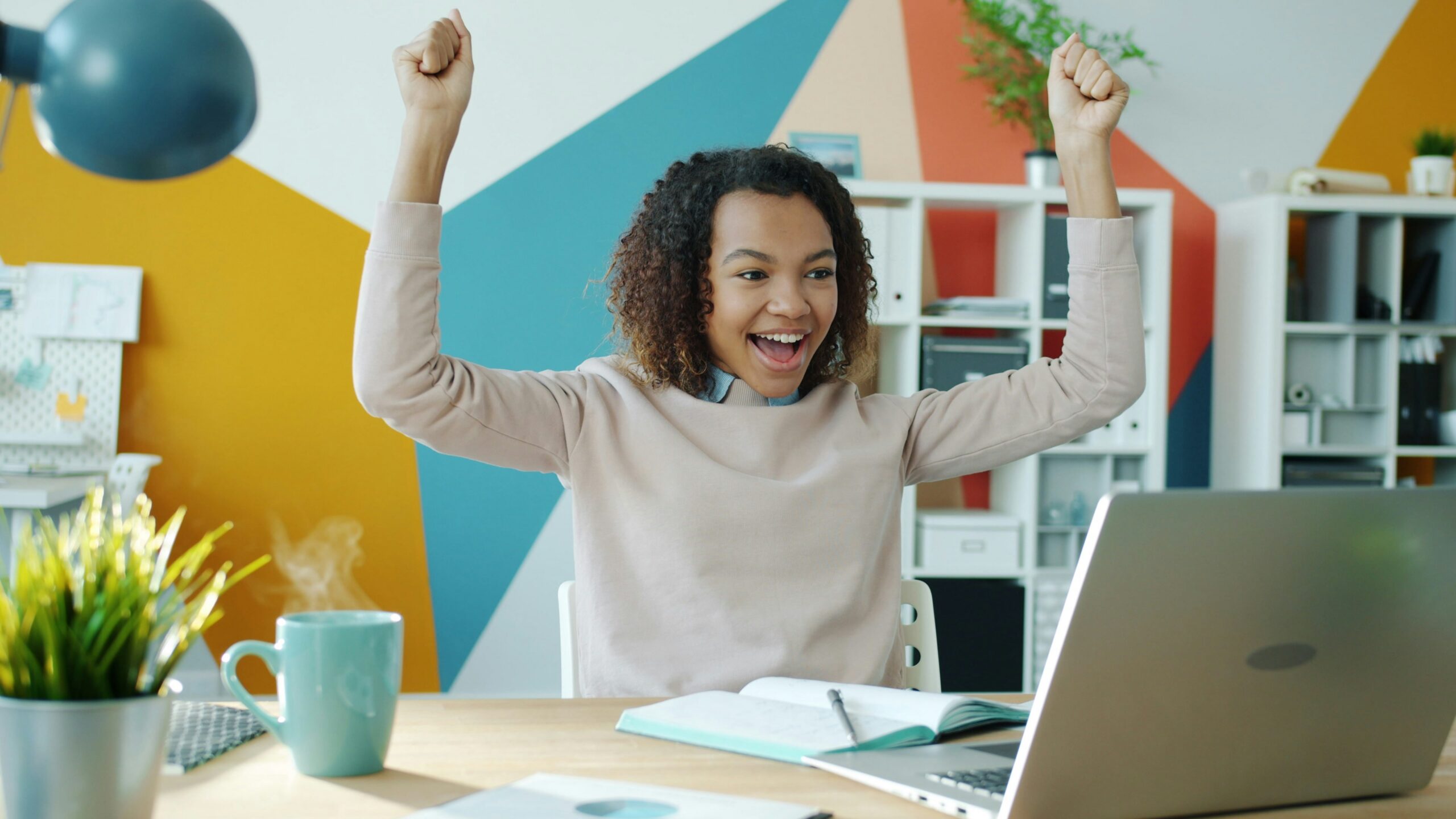 Happy student celebrating a scholarship approval at her desk.